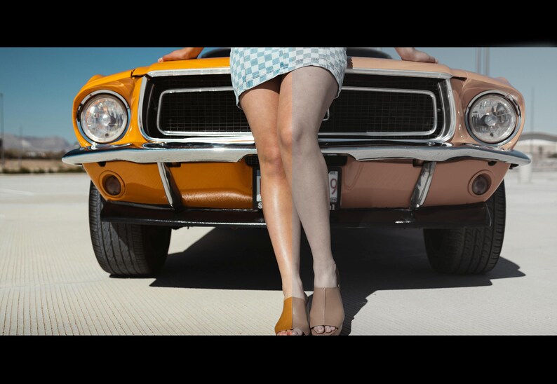 May include: A yellow classic car with a woman sitting on the hood. The woman is wearing a checkered skirt and white shoes.