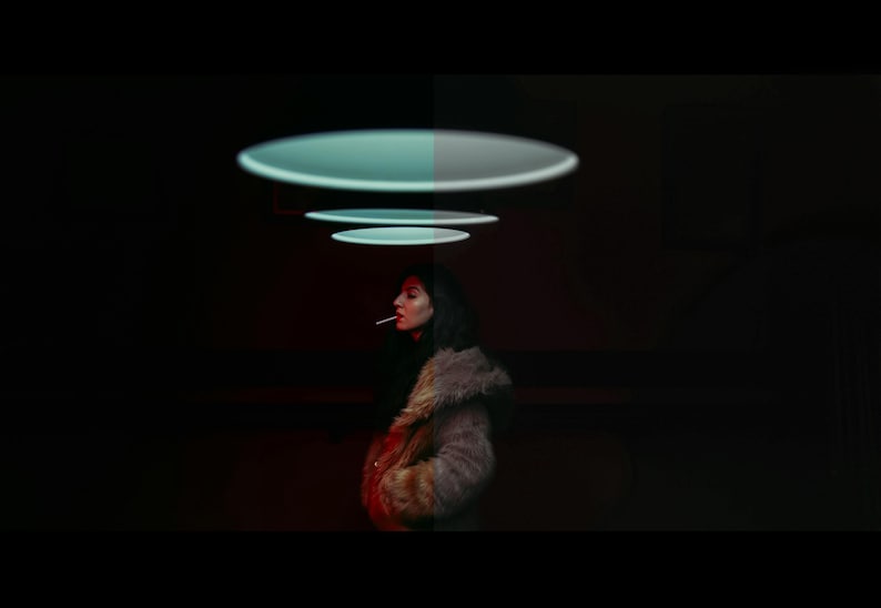 May include: A woman in a brown and black fur coat stands in a dark room with a series of glowing, circular lights above her head.