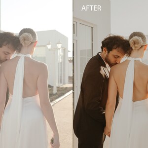 May include: A couple in wedding attire, the groom is kissing the bride's shoulder. The bride is wearing a white halter dress with a long flowing sash. The groom is wearing a black suit. The couple is standing in front of a white building with a door.