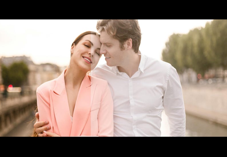 May include: A couple standing close together, looking at each other with smiles on their faces. The woman is wearing a pink blazer and the man is wearing a white button-down shirt. They are standing in front of a city background.