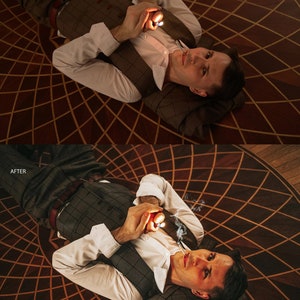 May include: A man in a white shirt and a brown plaid vest lies on a patterned wooden floor, holding a lighter and a cigarette in his hands. He is looking up at the camera.