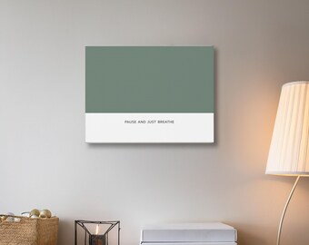 May include: A rectangular canvas art print with a sage green upper section and a white lower section. The text "PAUSE AND JUST BREATHE" is printed in black on the white section. The artwork is displayed on a light gray wall.