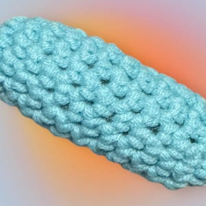 May include: A light blue crocheted object shaped like a long, thin cylinder. The object is made with a simple stitch pattern and has a smooth, textured surface.