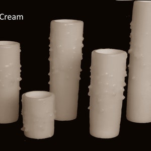 May include: Five cream-colored pillar candles with a textured surface. The candles are of varying heights.