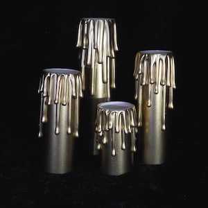 May include: Four gold-colored candle holders with dripping wax. The candle holders are cylindrical and have a smooth, metallic finish.