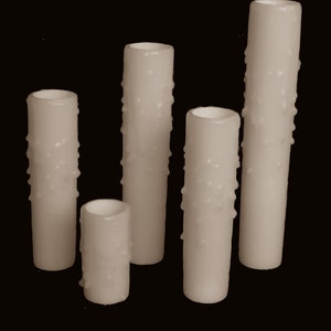 May include: Five white pillar candles with a textured surface. The candles are different sizes.