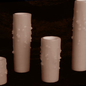 May include: Four honey-colored candles with a textured, star-shaped design. The candles are different sizes and are arranged in a row from tallest to shortest.