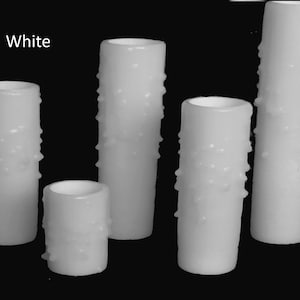 May include: Five white pillar candles with a textured surface. The candles are different sizes and are arranged in a row. The text "White" is visible in the top left corner of the image.