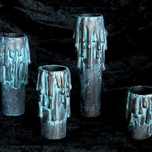 May include: Four teal and black candles with dripping wax. The candles are different sizes and are arranged in a row on a black surface.