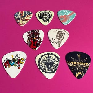 Peut inclure: Assortiment de 10 médiators de guitare avec différents motifs sur le thème du rock and roll. Les médiators sont blancs, noirs et crème avec des graphismes colorés. Certains des motifs incluent un microphone, un crâne, une guitare et les mots "Rock Forever".