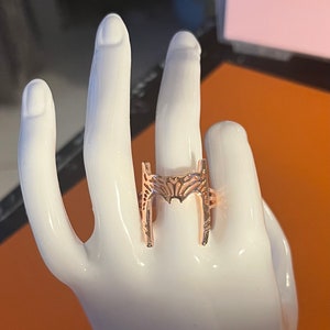 Op de afbeelding: Een ring van roségoud met een decoratief ontwerp in de vorm van de letter H.