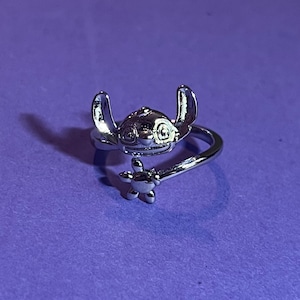 Peut inclure: Une bague en argent avec un personnage de dessin animé aux grandes oreilles et un motif floral. La bague est réglable et peut être portée à n'importe quel doigt.