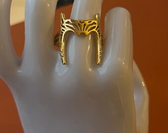 May include: A gold ring with a detailed, intricate design resembling a crown or a stylized animal head.