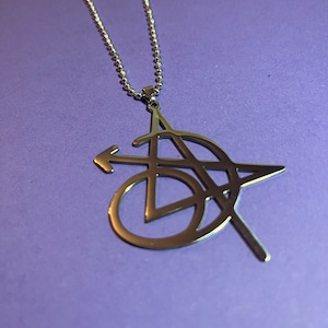 May include: A silver necklace with a pendant featuring a stylized geometric design. The pendant is made of metal and has a shiny finish.