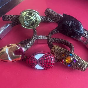 May include: Four braided leather bracelets with metal charms featuring Marvel characters. The charms include Iron Man, Spider-Man, Doctor Strange and Black Panther. The Infinity Gauntlet charm has the inscription "Infinity Gauntlet".