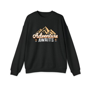 Könnte beinhalten: Schwarzer Pullover mit einem Bergketten-Motiv und dem Text "Adventure Awaits" in Orange und Weiß.
