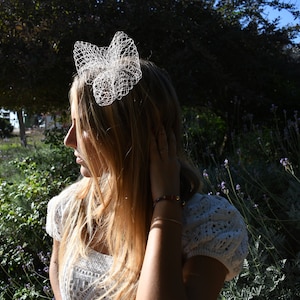 Può includere: Una donna con lunghi capelli biondi indossa una fascia per capelli in pizzo bianco con un fiocco a forma di farfalla.