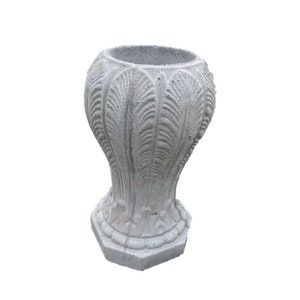 May include: A gray concrete planter with a decorative, leaf-like design. The planter has a wide, round top and a hexagonal base.
