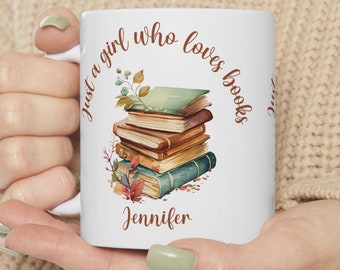 Op de afbeelding: Een witte keramische mok met een stapel kleurrijke boeken en bloemaccenten. De tekst "Just a girl who loves books" staat in een gebogen bruin lettertype boven de boeken en de naam "Jennifer" is in het bruin onder de stapel gedrukt.
