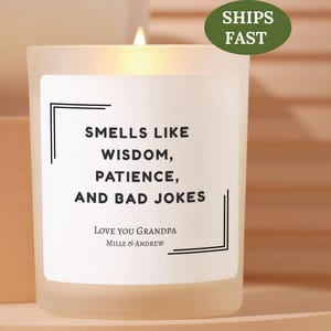 May include: A lit, frosted glass candle with a white label. The label reads "SMELLS LIKE WISDOM, PATIENCE, AND BAD JOKES. LOVE YOU GRANDPA, MILLE & ANDREW." A green oval sticker says "SHIPS FAST."