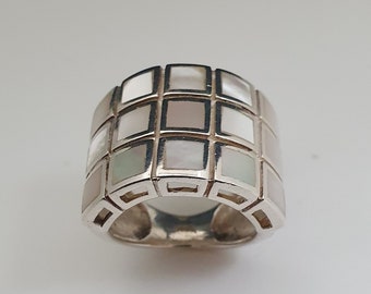 May include: A silver ring with a wide band featuring a geometric pattern of white mother-of-pearl squares.
