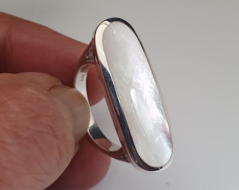 Könnte beinhalten: Ein silberner Ring mit einem großen ovalen, weißen Perlmuttstein.
