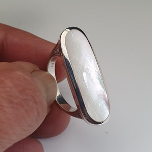 Pode incluir: Um anel de prata com uma grande pedra oval de madrepérola branca.
