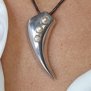 Pode incluir: Um colar com um pingente de garra de prata com quatro pérolas brancas em um cordão preto.