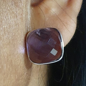 Op de afbeelding: Een paar zilveren oorbelletjes met een vierkante amethist edelsteen.