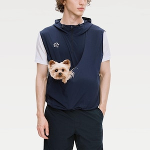 Könnte beinhalten: Marineblaue Kapuzenweste mit einer Tasche zum Tragen eines kleinen Hundes. Die Weste hat einen Reißverschluss und ein kleines Logo auf der Brust. Ein kleiner, hellbrauner Hund schaut aus der Tasche.