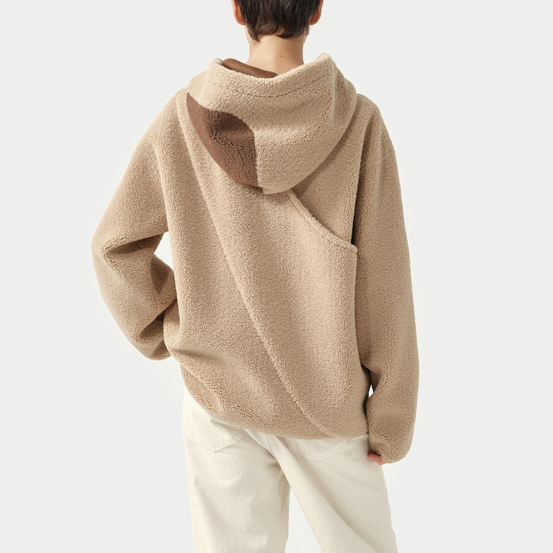 Pu&ograve; includere: Una felpa con cappuccio in pile color cammello con un accento marrone sul cappuccio. La felpa con cappuccio ha una tasca a marsupio e maniche lunghe. La modella indossa pantaloni bianchi sporchi. La felpa &egrave; realizzata in un materiale morbido e strutturato.