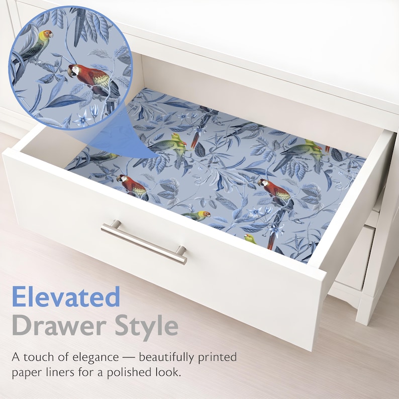 May include: An open white drawer displays a drawer liner with a blue floral and bird design. The liner showcases parrots and foliage. The text "Elevated Drawer Style" and a description are visible.