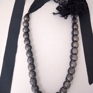 Puede incluir: Un collar de cinta negra con un acento de flor de encaje negro y cuentas plateadas.