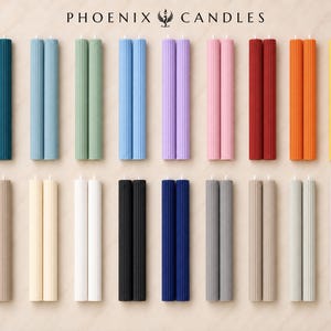 a collection of 16 candles in various colors and shapes, arranged in a grid-like pattern on a light-colored background.