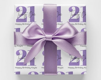 May include: A wrapped gift with a white background and a repeating pattern of the number "21" and the words "Twenty One". The gift is tied with a lavender satin ribbon and bow. The text "Happy Birthday Kayla" is also printed on the wrapping paper.