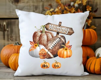 May include: White throw pillow with a football, pumpkins, and a sign that says "Mommy". The pumpkins are decorated with leopard print and sunflowers. The pillow also has the names "Alex" and "Leo" written on it.