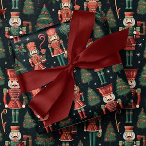 May include: A wrapped gift with a burgundy bow sits atop wrapping paper patterned with red and green nutcrackers and Christmas trees on a dark background. Decorative red star and flower accents are also present.