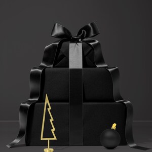 May include: A stack of wrapped black gift boxes with a large black satin bow and ribbon. A gold-colored metal Christmas tree and a black ornament with a gold top are in front of the gifts. The background is a dark gray.