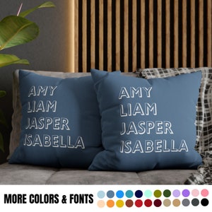 May include: Two blue throw pillows with white text that reads "AMY LIAM JASPER ISABELLA". The pillows are on a couch with a patterned throw blanket.