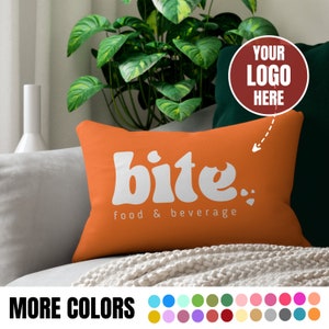 May include: Orange rectangular pillow with the word "bite" in white, along with "food & beverage" underneath. The pillow is on a gray couch with a white blanket. The image also includes a plant and a color palette.