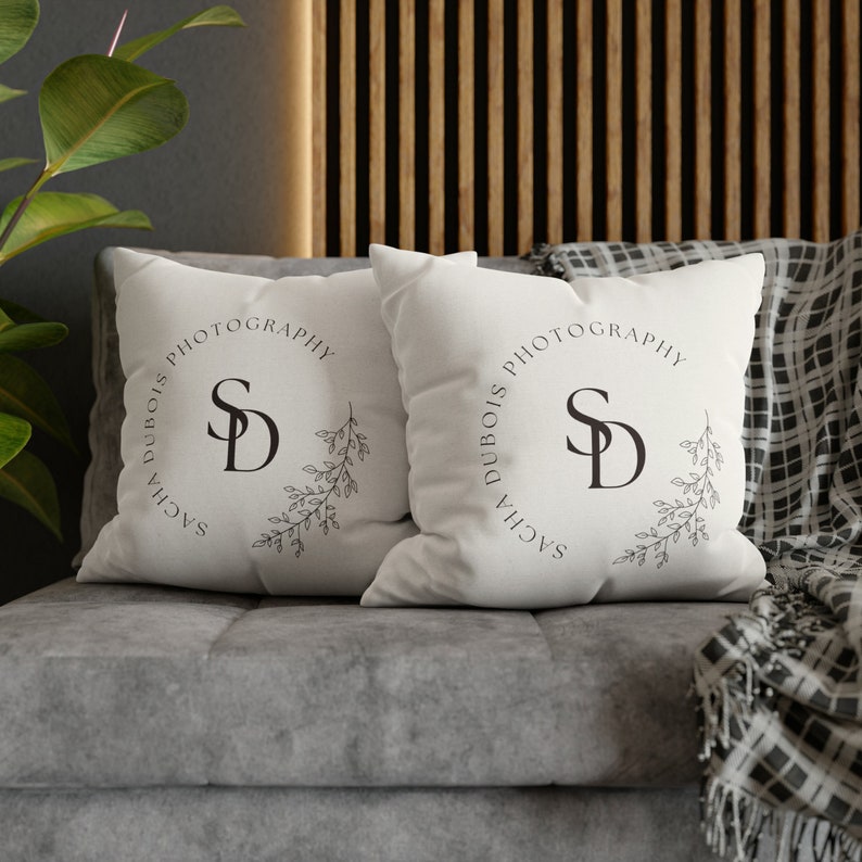 May include: Two white throw pillows with black text and a floral design. The text on the pillows reads "Sacha Dubois Photography" and features the initials "SD" in a circle.