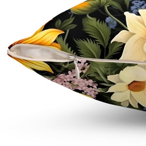 Puede incluir: Un primer plano de una almohada con cierre de cremallera. La almohada est&aacute; hecha de una tela suave y presenta un estampado floral con girasoles, flores blancas y hojas verdes sobre un fondo negro.