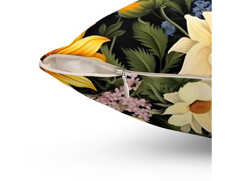 Puede incluir: Un primer plano de una almohada con cierre de cremallera. La almohada est&aacute; hecha de una tela suave y presenta un estampado floral con girasoles, flores blancas y hojas verdes sobre un fondo negro.