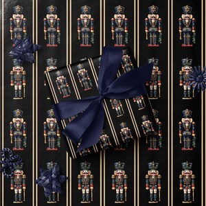 May include: A wrapped gift with a navy blue bow sits on a black background with vertical white stripes. The wrapping paper features a repeating pattern of toy nutcracker soldiers in blue, red, and gold. Decorative navy blue accents are scattered around the gift.