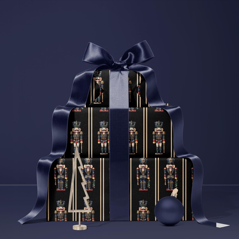 May include: A stack of wrapped gifts with a navy blue ribbon and bow. The wrapping paper features a repeating pattern of nutcracker soldiers on a black background with gold stripes. A small gold Christmas tree and a blue ornament are also present.