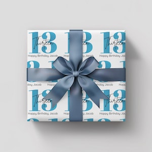 Pode incluir: Presente embrulhado em papel branco com um padr&atilde;o repetido do n&uacute;mero 13 em azul, a palavra "Thirteen" e o texto "Happy Birthday Jacob". O presente &eacute; amarrado com uma fita e la&ccedil;o de cetim azul.