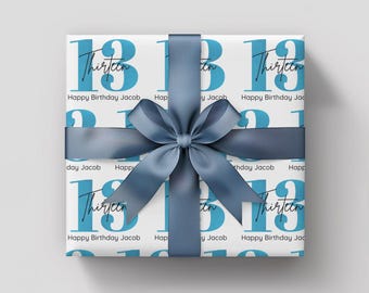 May include: Gift-wrapped present with a white background and a repeating pattern of the number 13 in blue, with the word "Thirteen" and "Happy Birthday Jacob" printed on the wrapping paper. A blue satin ribbon and bow complete the gift.