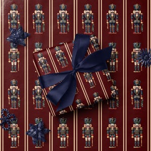 May include: A wrapped gift with a navy blue bow sits on a background of burgundy wrapping paper with vertical stripes. The wrapping paper features a repeating pattern of nutcracker soldiers in blue, red, and gold.