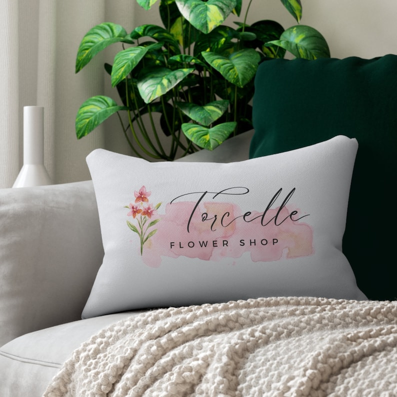 Pode incluir: Travesseiro branco com um design de aquarela rosa e o texto "Torcelle Flower Shop" em escrita cursiva preta.