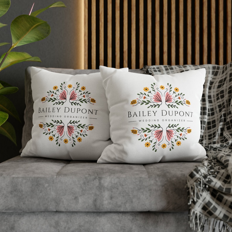 May include: Two white throw pillows with floral designs and the text "Bailey Dupont - Wedding Organizer" on a gray couch.